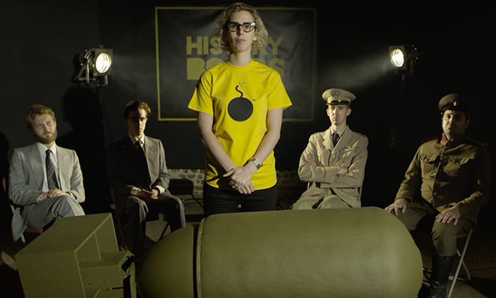 World War 2 Atomic bomb video scene with female presenter wearing History Bomb t-shirt standing in front of 4 commanding officers.